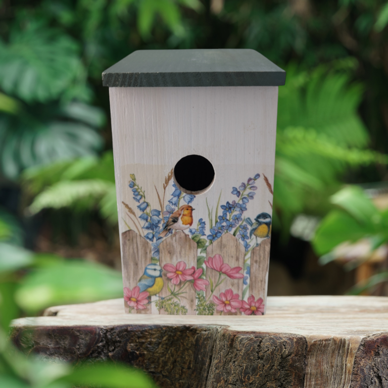 Birdhouse adorned with small garden birds, surrounded by purple blooms and trees in bloom.